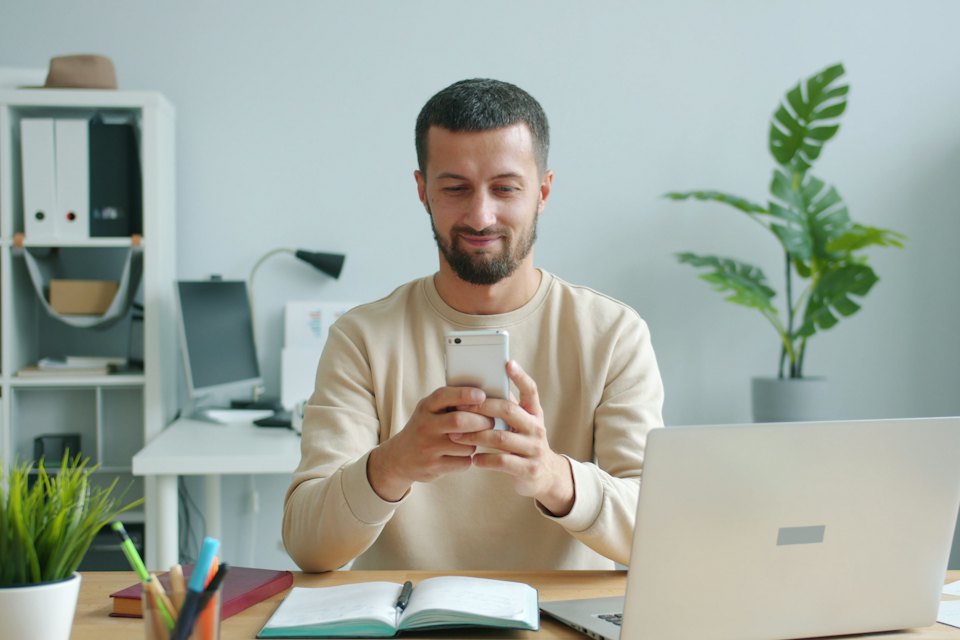 Un collaborateur sourit en écrivant sur son téléphone, à son bureau